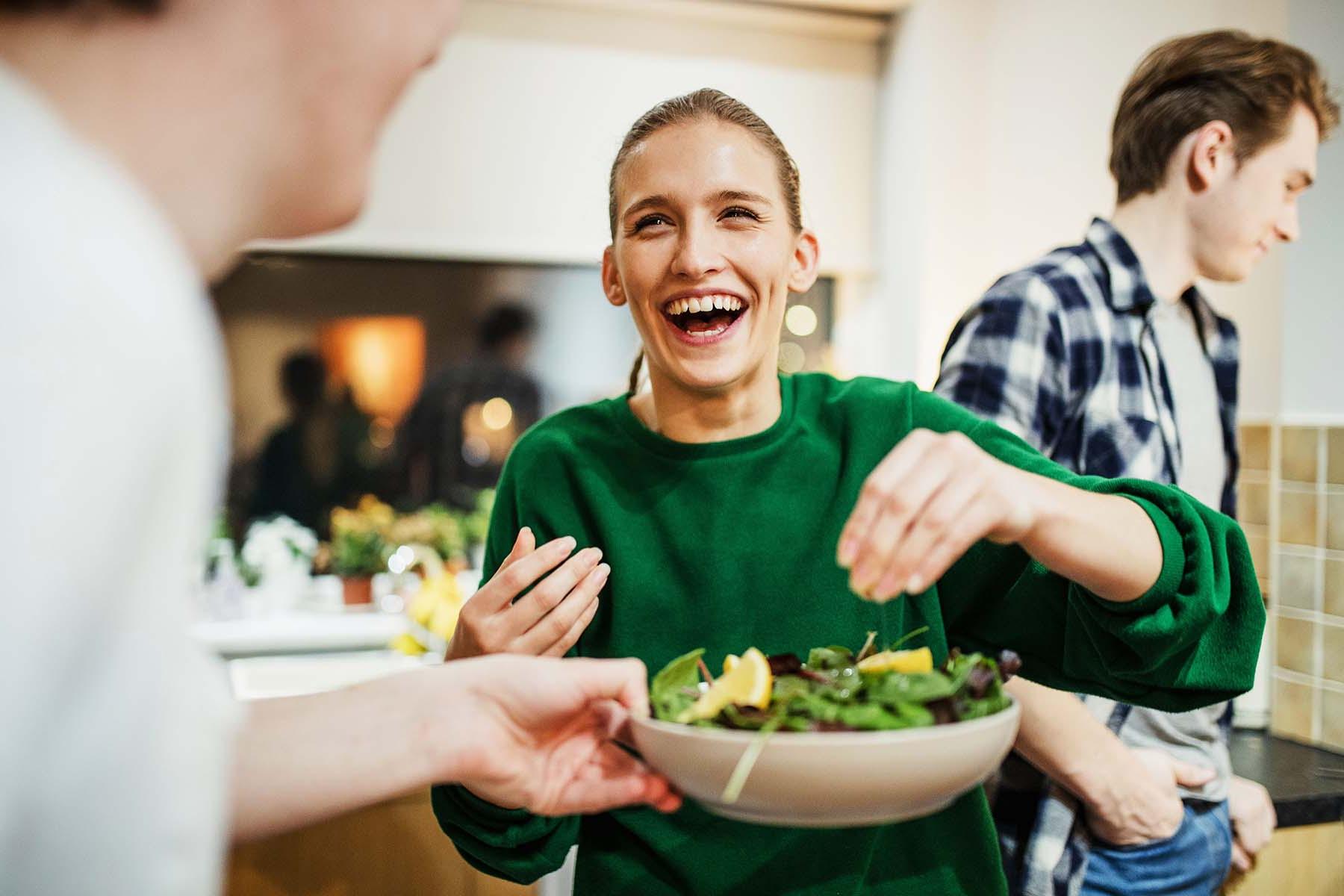 Laughing woman serving salad with people in the background.